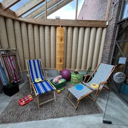 Tweedehands tuinmeubelen: ligbedden met blauw-witte strepen, paarse bal, groene emmer en ander tuingereedschap op betonvloer