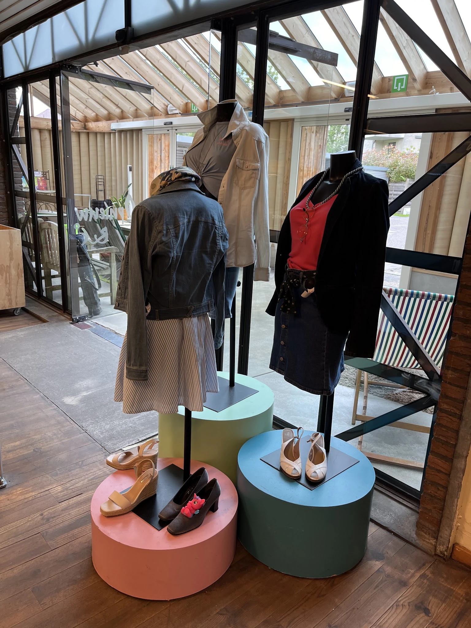 Etalage met kledingmanequins: zwart leren jack met beige plissérok, zwart wollen jas met rood topje, en bruine schoenen op di