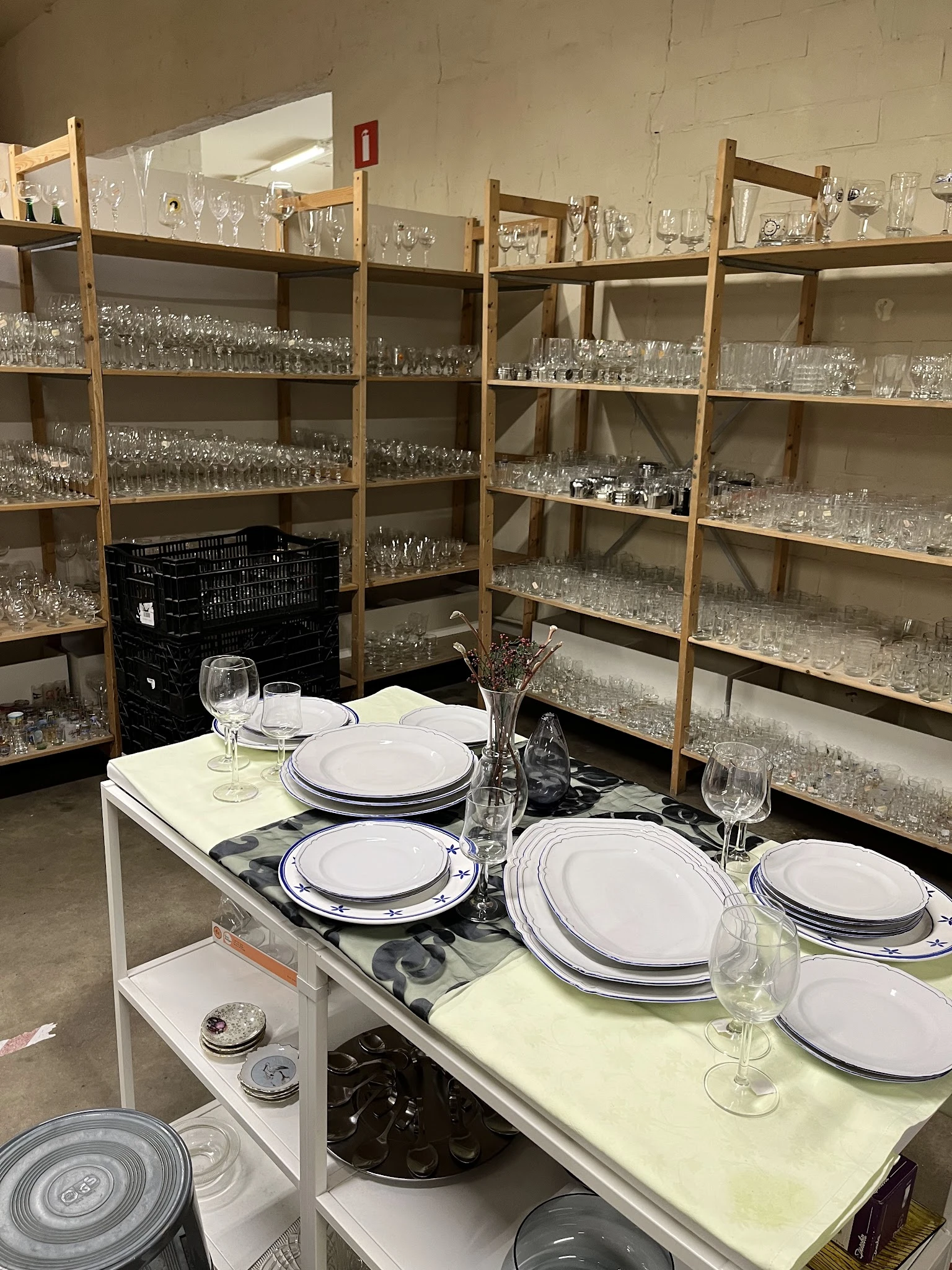 Tafelschikking met borden, glazen en bestek op een display tafel, met achterin volle stellingen met serviesgoed