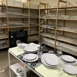 Tafelschikking met borden, glazen en bestek op een display tafel, met achterin volle stellingen met serviesgoed