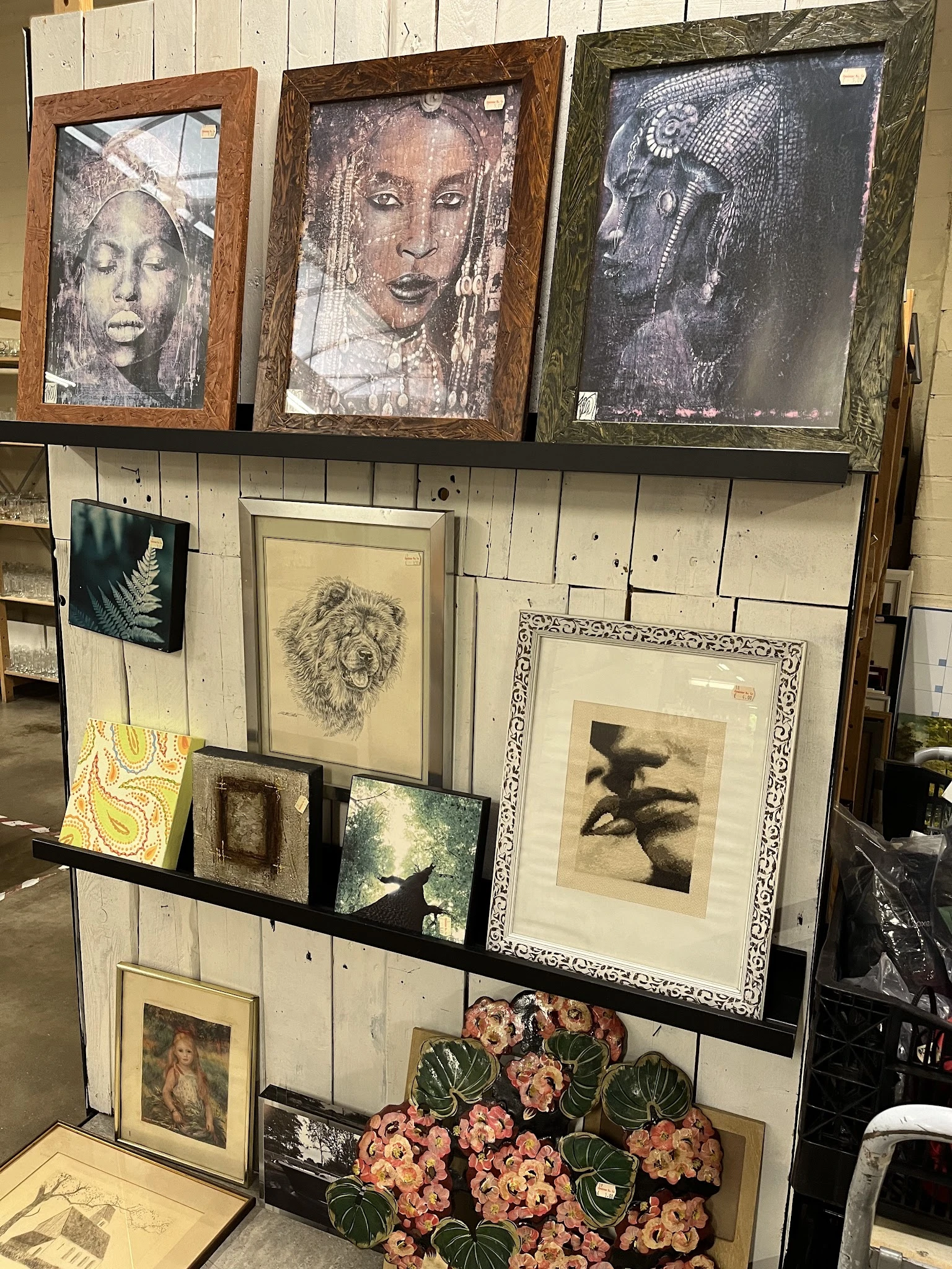 Uitgestalde kunstprenten en tekeningen in verschillende formaten en lijsten tegen een houten wand