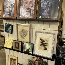 Uitgestalde kunstprenten en tekeningen in verschillende formaten en lijsten tegen een houten wand