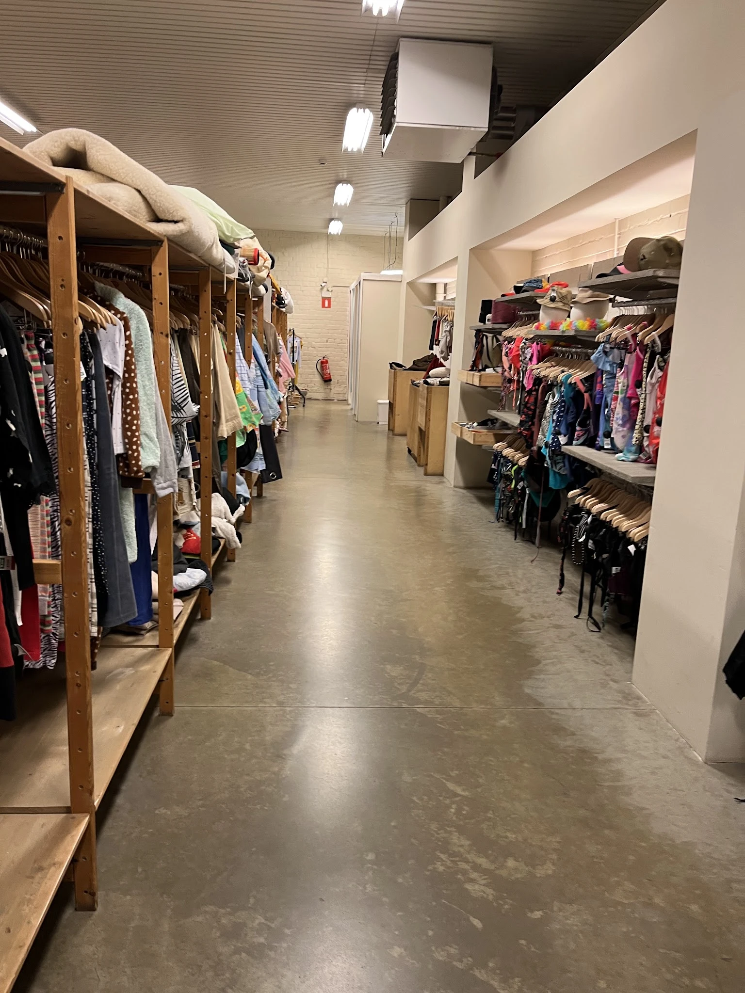 Winkelgang met houten stellingen vol tweedehands kleding aan beide zijden