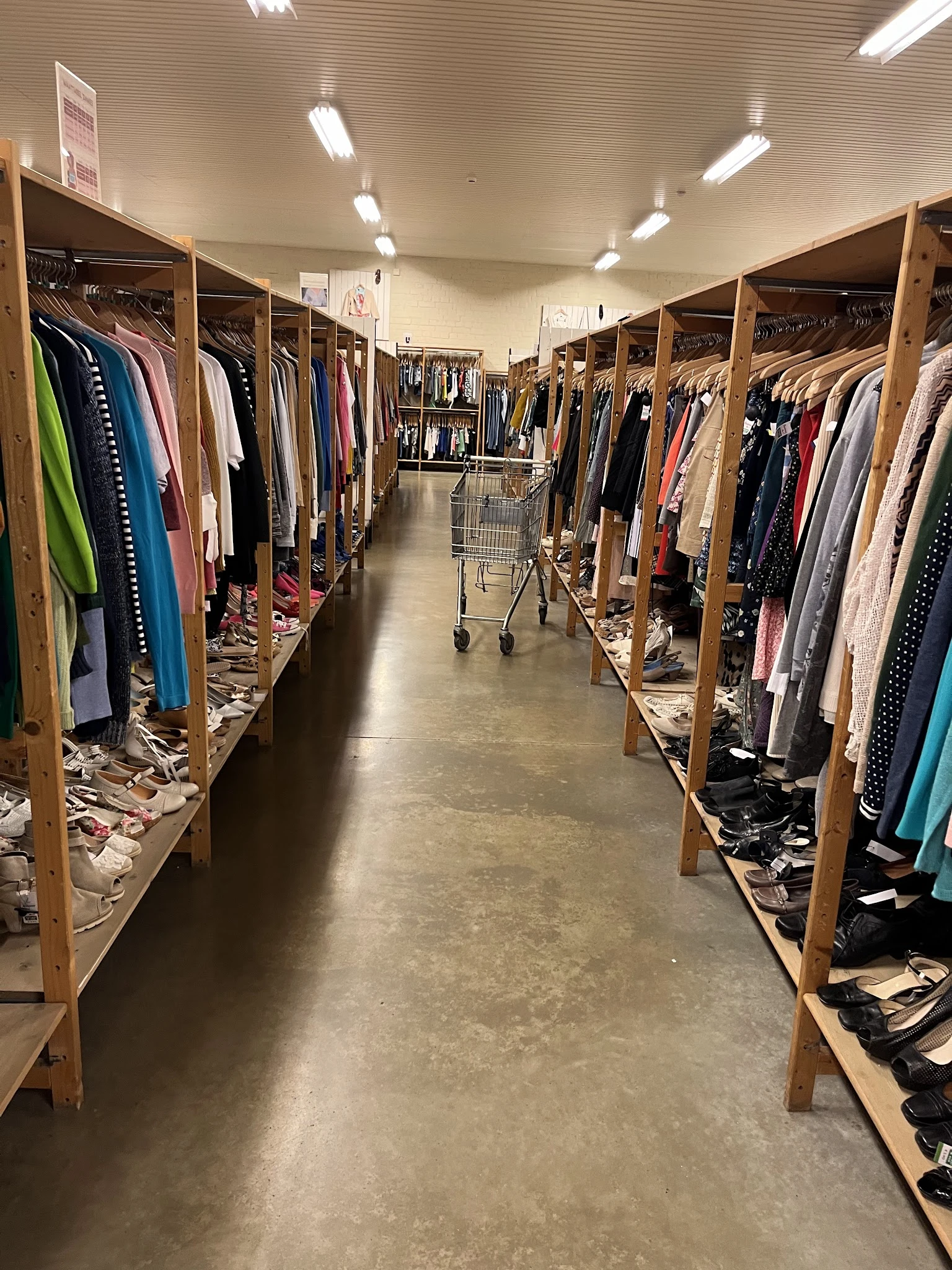 Gangpad tussen houten rekken vol tweedehands kleding in verschillende kleuren