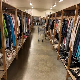 Gangpad tussen houten rekken vol tweedehands kleding in verschillende kleuren