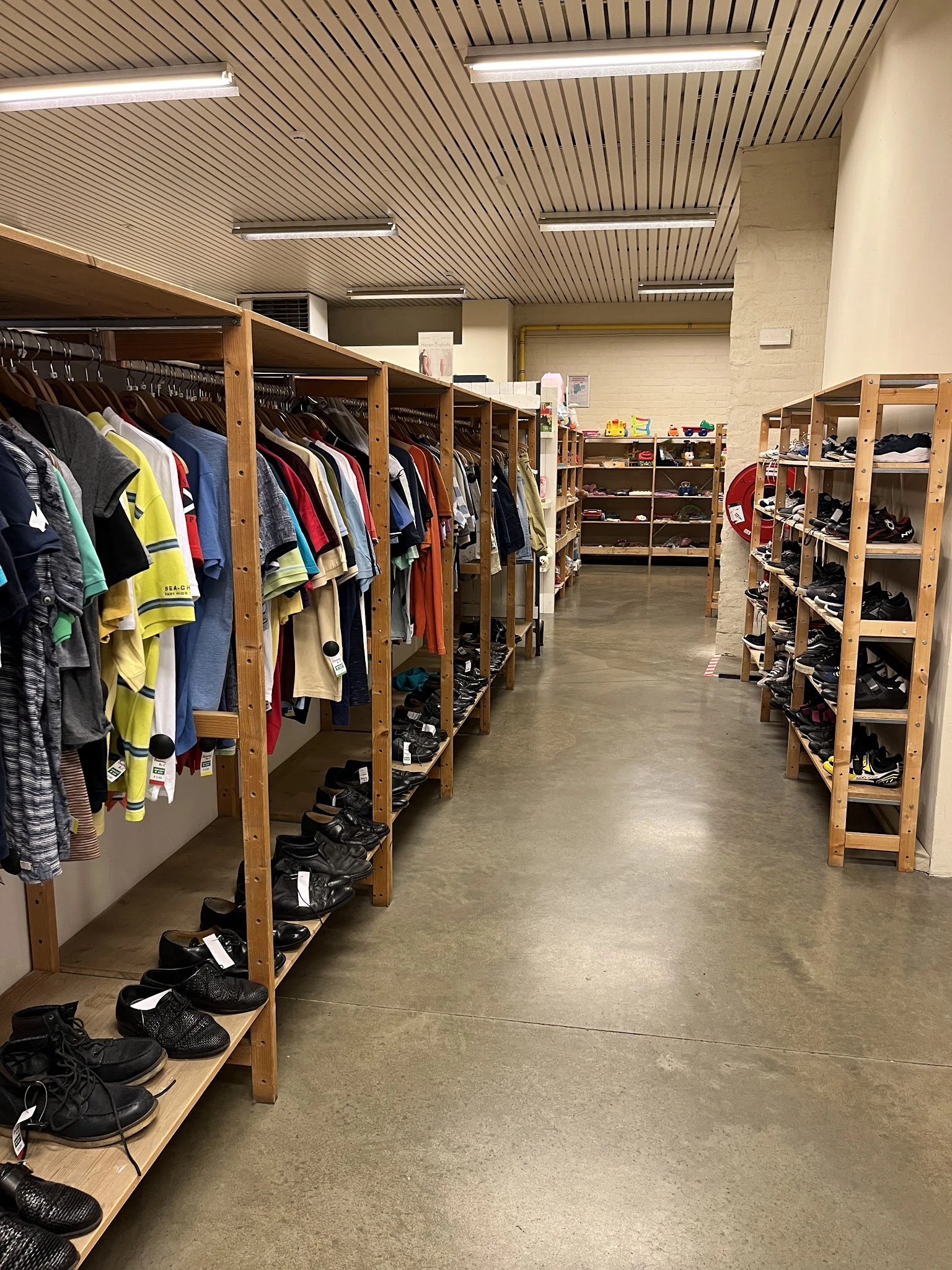 Winkelinterieur met houten stellingen vol kleding aan hangers en schoenen in bakken