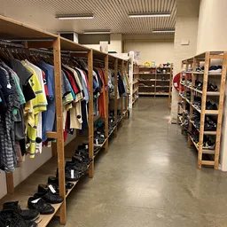Winkelinterieur met houten stellingen vol kleding aan hangers en schoenen in bakken