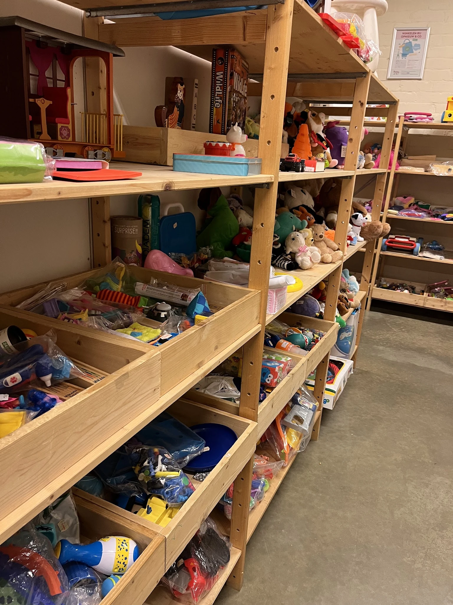 Houten stellingen met speelgoed, knuffels, boeken en diverse tweedehands artikelen in de winkel
