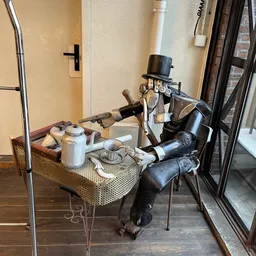 Decoratieve robot-figuur in zwart metaal met hoed zittend aan een tafeltje met vintage huisraad