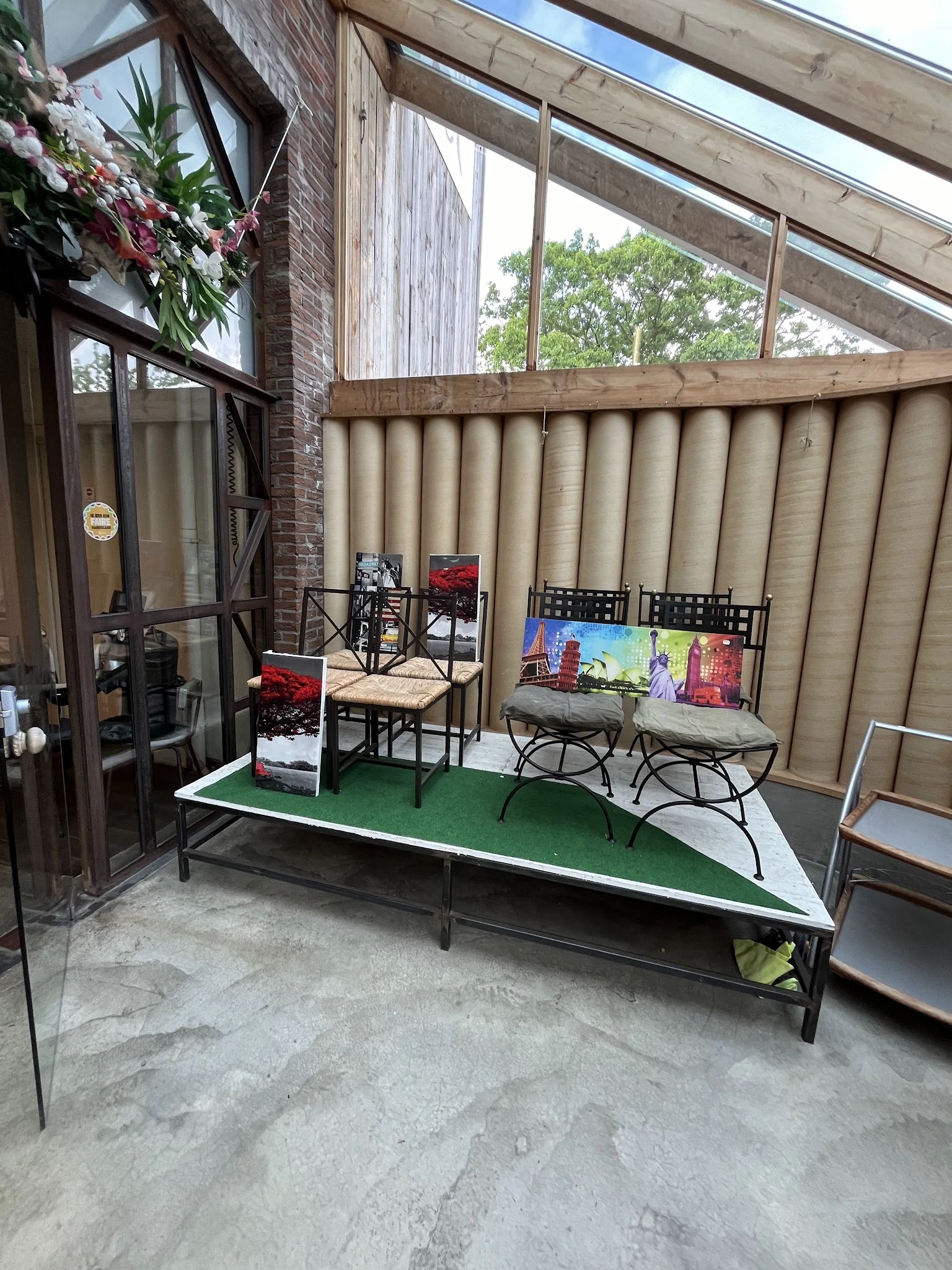 Terras of uitstalkamer met groene vloer, stoelen, tafels en displays tegen muren met beige gordijnen