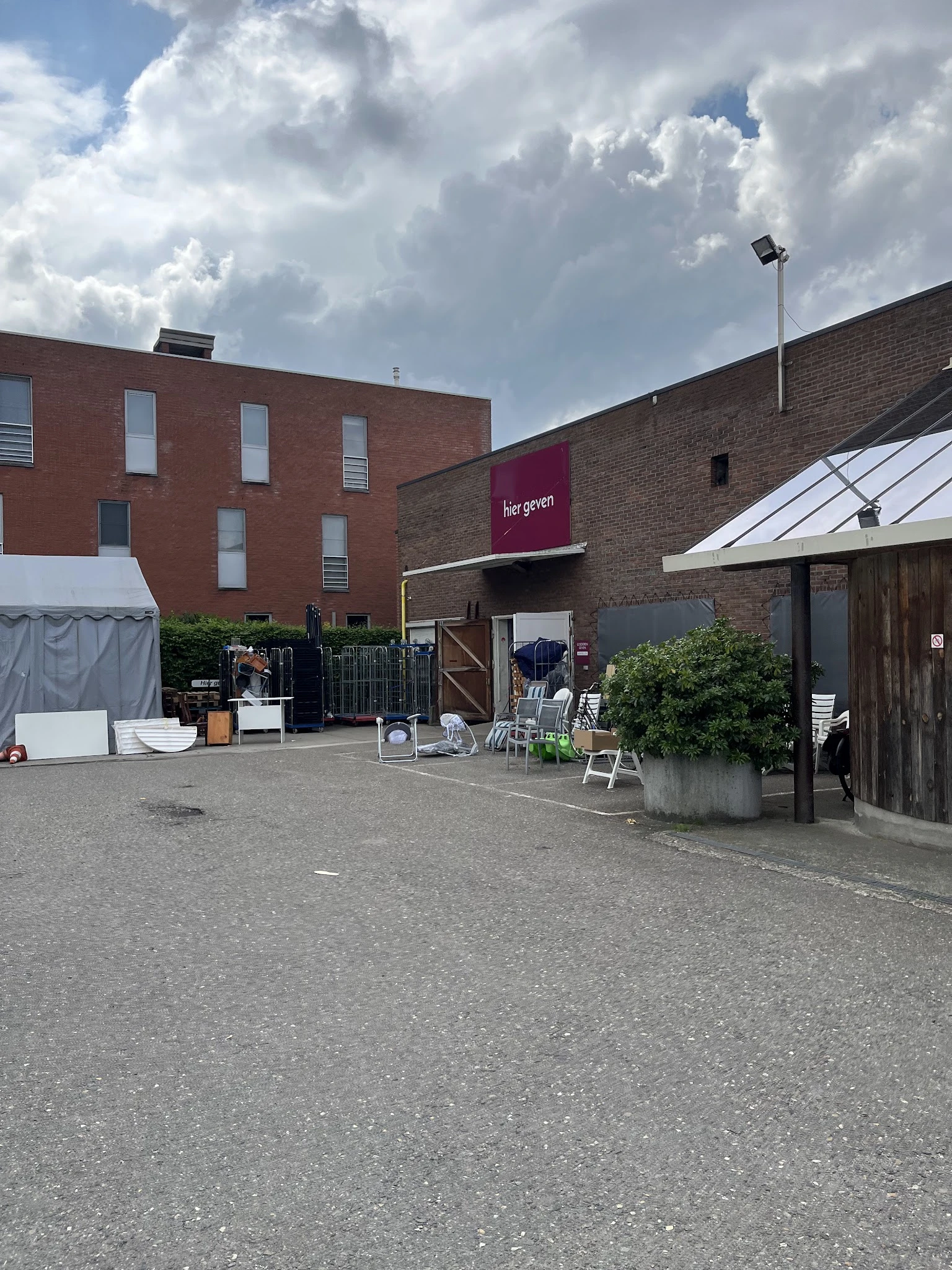 Voorkant van kringloopwinkel met bakstenen gevel, terras met stoelen en witte tent links
