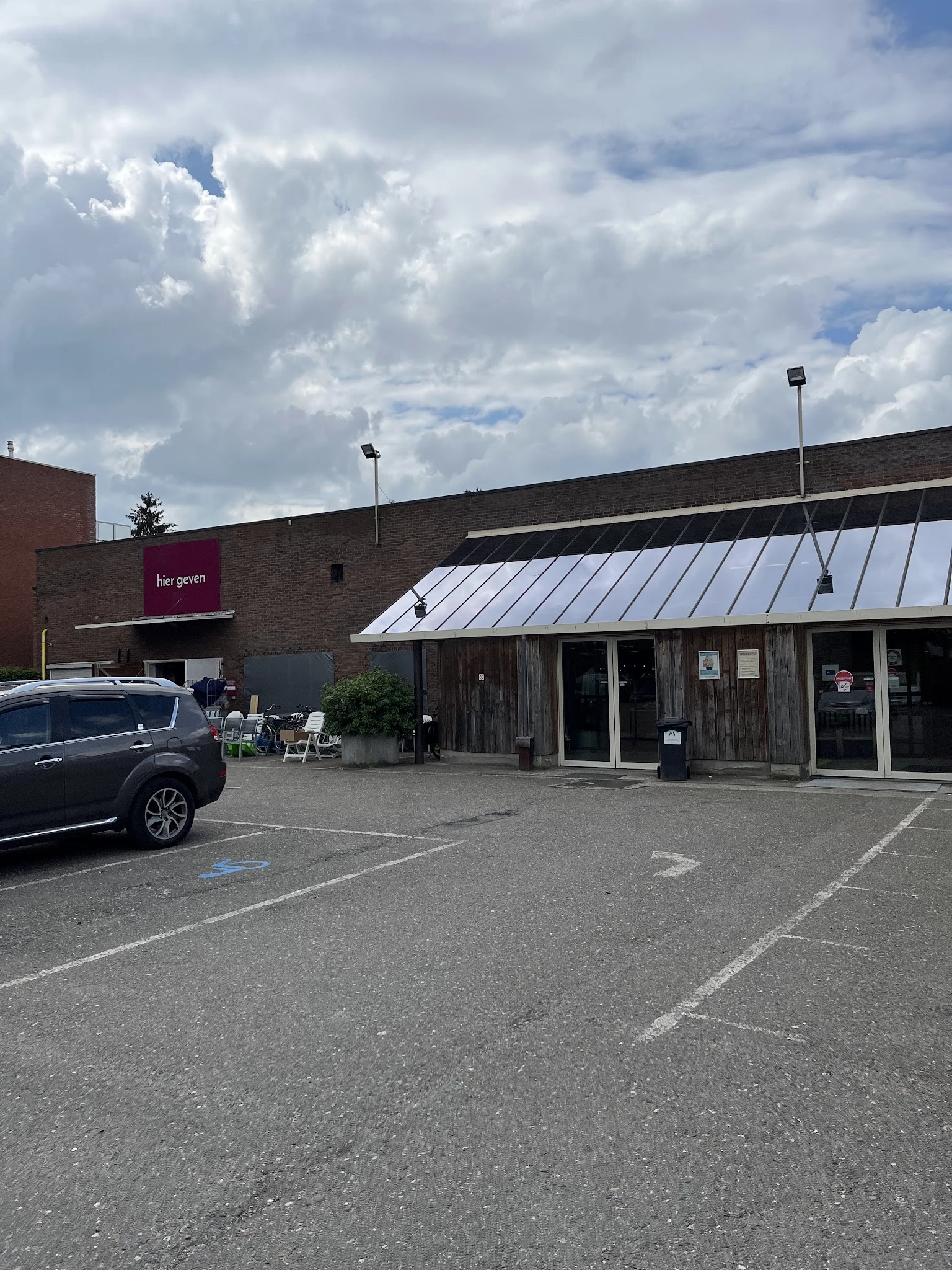 Exterieur van kringloopwinkel met bakstenen gevel, houten luifel en parkeerplaats