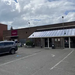 Exterieur van kringloopwinkel met bakstenen gevel, houten luifel en parkeerplaats
