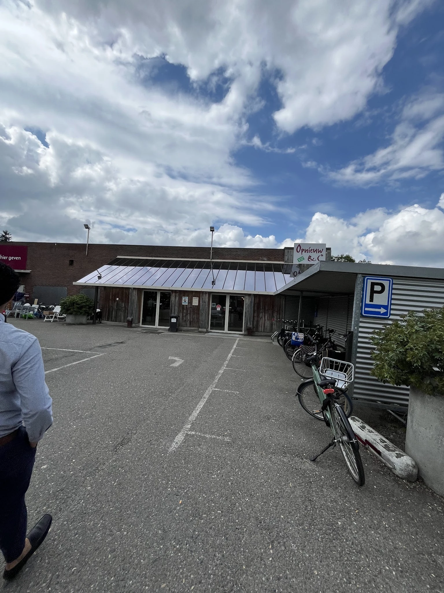 Voorkant kringloopwinkel met metalen dak, glazen deuren en parkeerplaats met fietsen