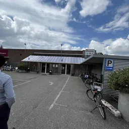 Voorkant kringloopwinkel met metalen dak, glazen deuren en parkeerplaats met fietsen