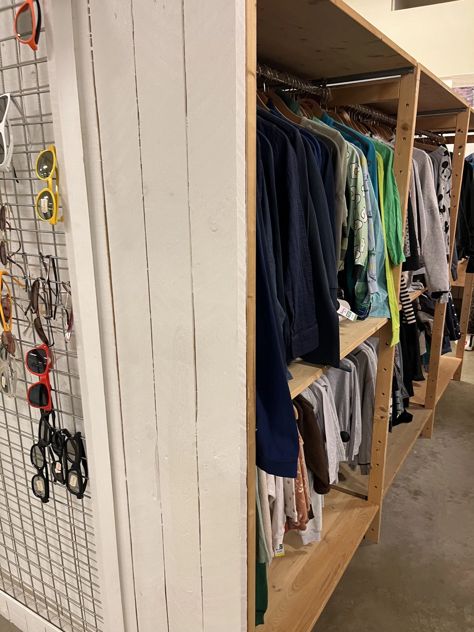 Houten rekken met tweedehands kleding in verschillende kleuren, waaronder donkerblauwe en groene kledingstukken