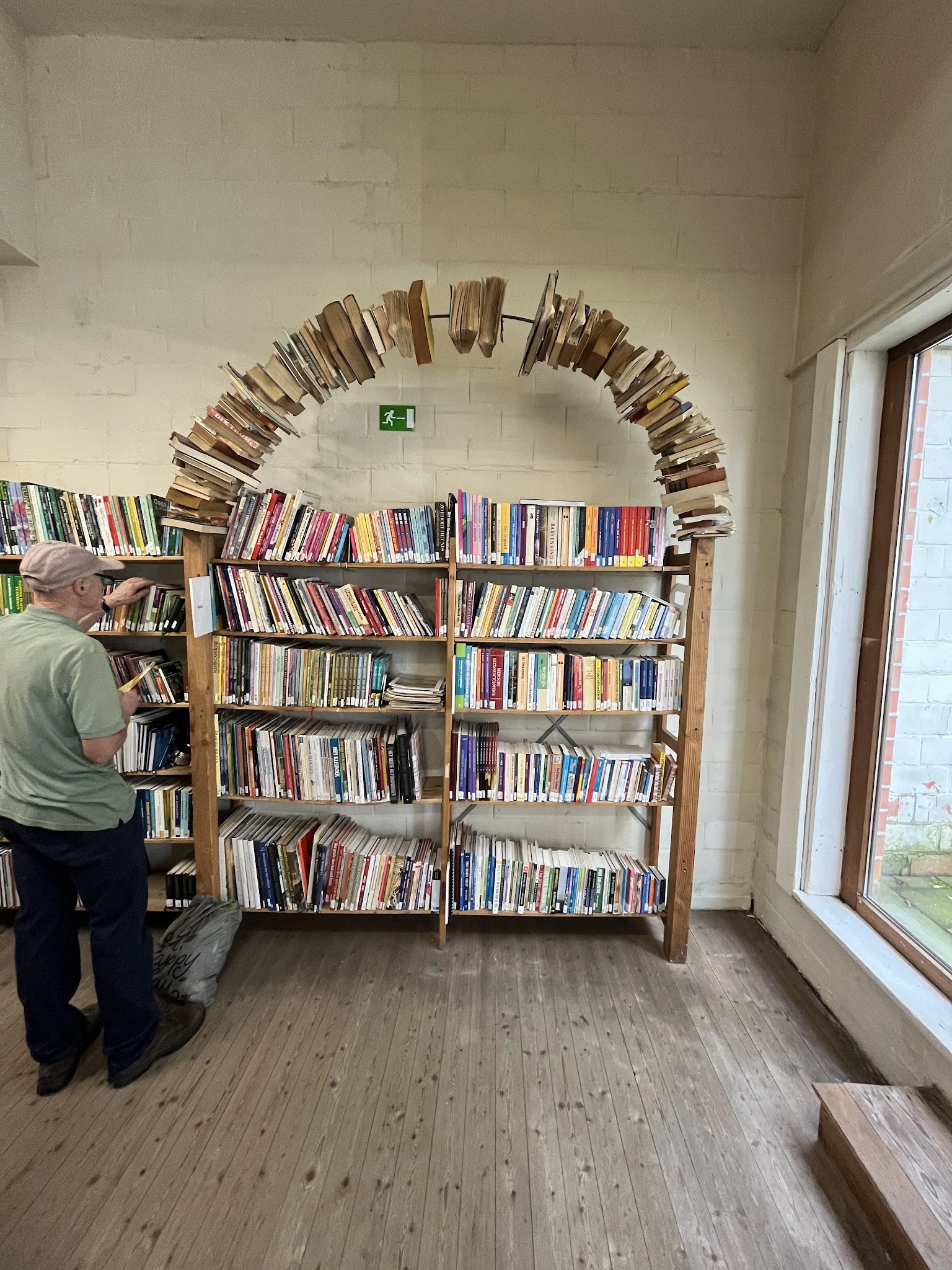 Boekenrekken met DVDs en boeken, met daaroven een decoratieve boekenslinger. Een klant bekijkt de collectie.