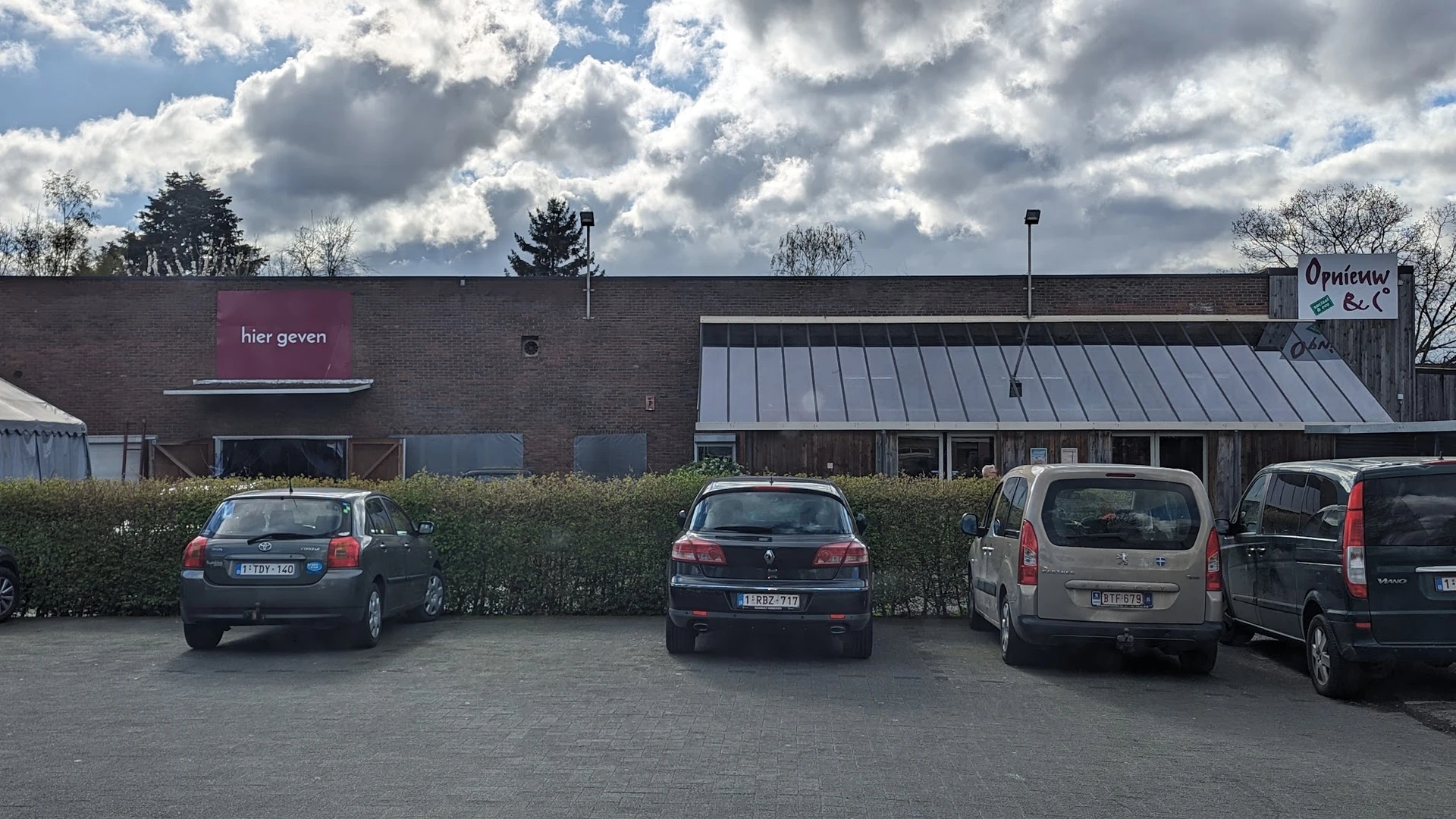 Voorgevel van kringloopwinkel met parkeerplaats en geparkeerde auto's