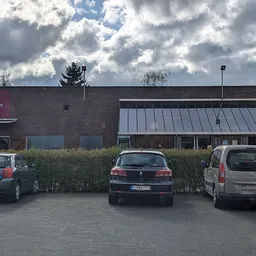 Voorgevel van kringloopwinkel met parkeerplaats en geparkeerde auto's