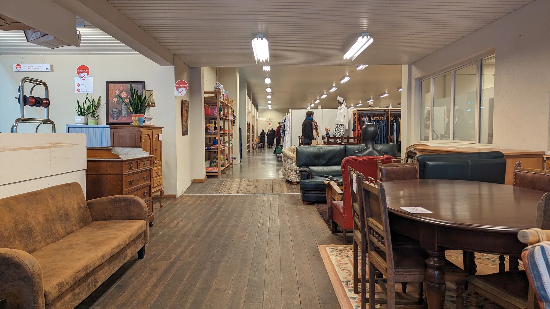 Ruim winkelinterieur met houten meubels, kleding en diverse tweedehands artikelen langs de wanden