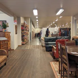 Ruim winkelinterieur met houten meubels, kleding en diverse tweedehands artikelen langs de wanden