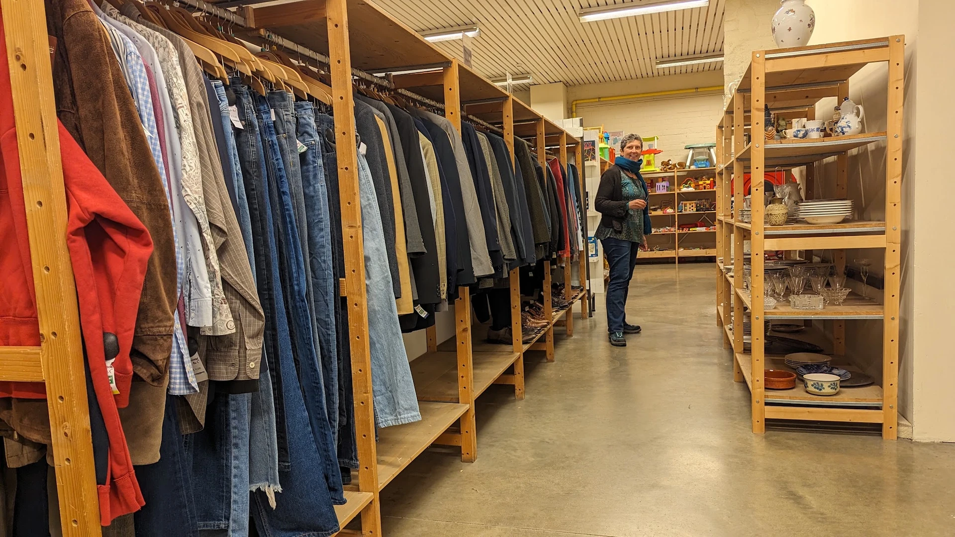 Winkelinterieur met houten stellingen vol tweedehands kleding en een bezoeker die rondkijkt