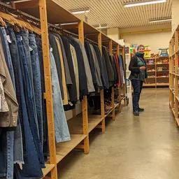 Winkelinterieur met houten stellingen vol tweedehands kleding en een bezoeker die rondkijkt