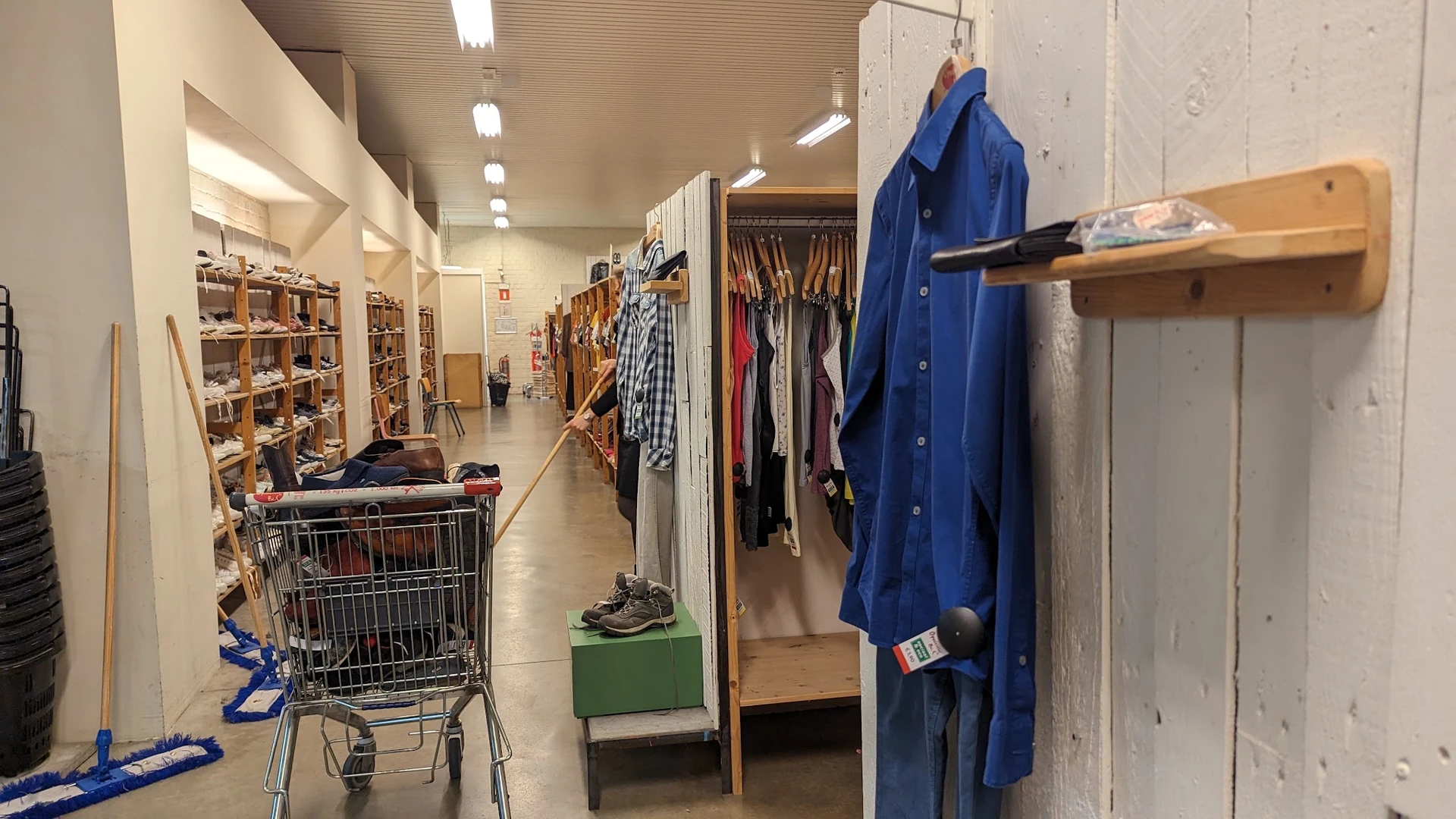 Winkelinterieur met kledingrekken, stellingen en een winkelwagen met spullen