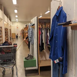 Winkelinterieur met kledingrekken, stellingen en een winkelwagen met spullen