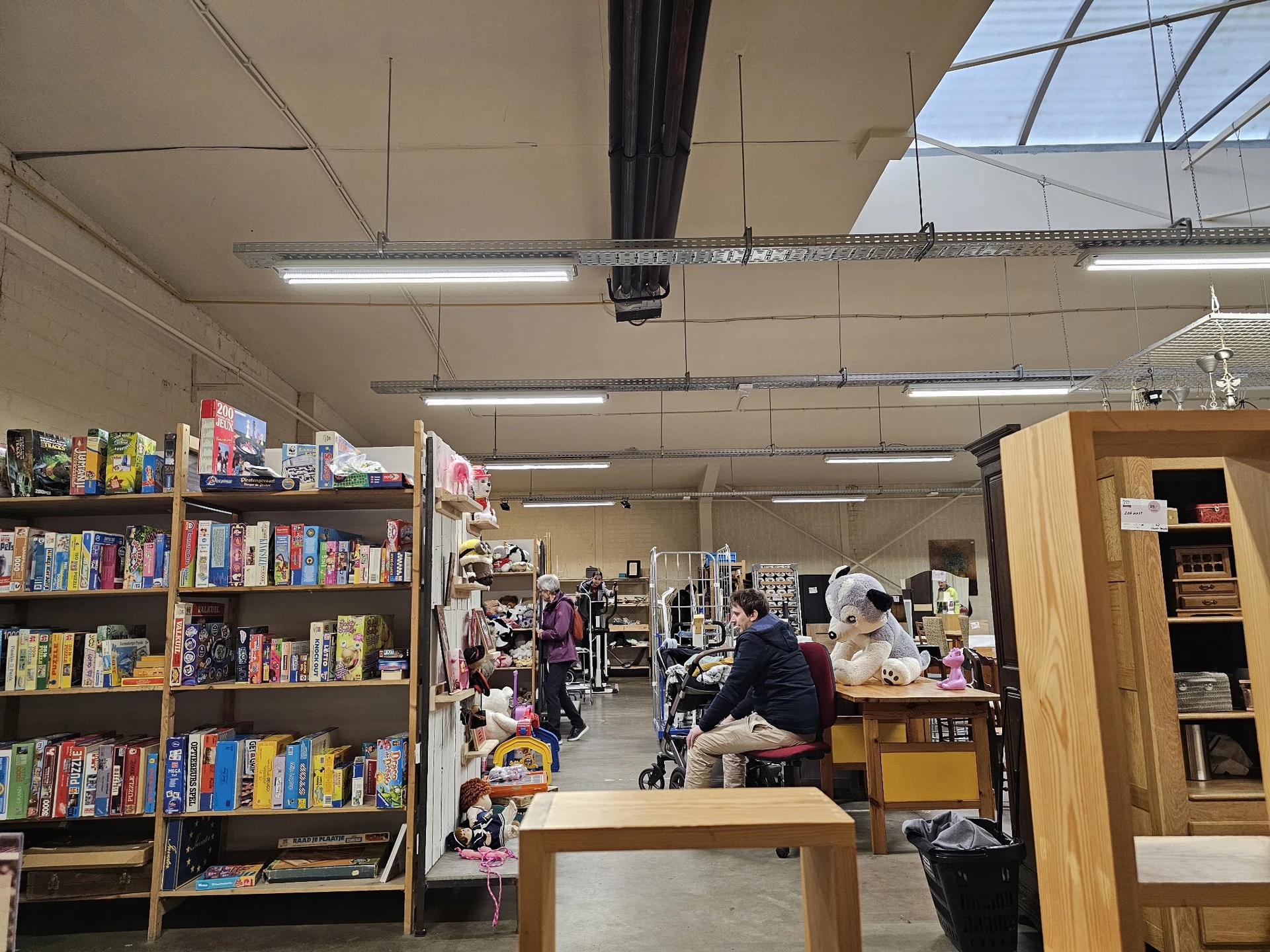 Overzicht van de winkelvloer met boekenrekken aan de linkerkant, kleding en diverse spullen in het midden, en houten kastjes 