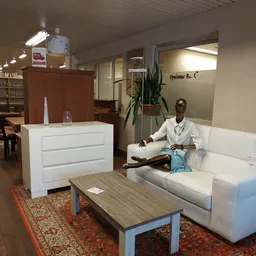 Showroom van kringloopwinkel met witte kast, houten tafel, witte bank en pop-upfiguur, plant en winkelinrichting zichtbaar