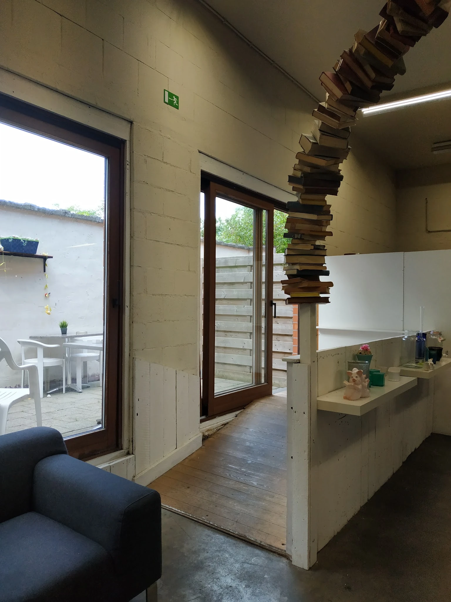 Binnenzicht van kringloopwinkel met open deuren naar terras, stellingen en een stapel boeken aan het plafond