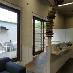 Binnenzicht van kringloopwinkel met open deuren naar terras, stellingen en een stapel boeken aan het plafond