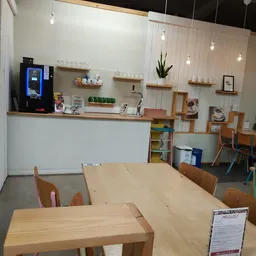 Kringloopwinkel interieur met houten tafels, stoelen, houten wandrekken, plantenbak en koffiemachine