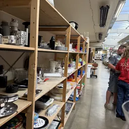 Houten stellingen met diverse huishoudelijke items en serviesgoed in een kringloopwinkel