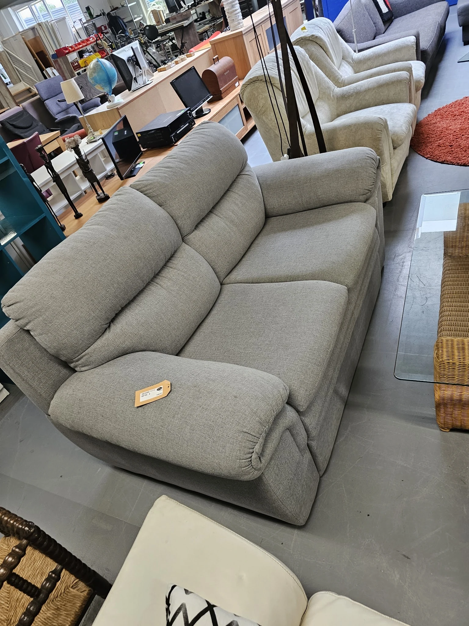 Grijze gestoffeerde fauteuil met kussen, gezien vanaf schuin boven in een kringloopwinkel