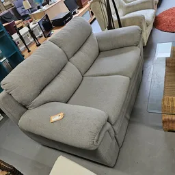 Grijze gestoffeerde fauteuil met kussen, gezien vanaf schuin boven in een kringloopwinkel