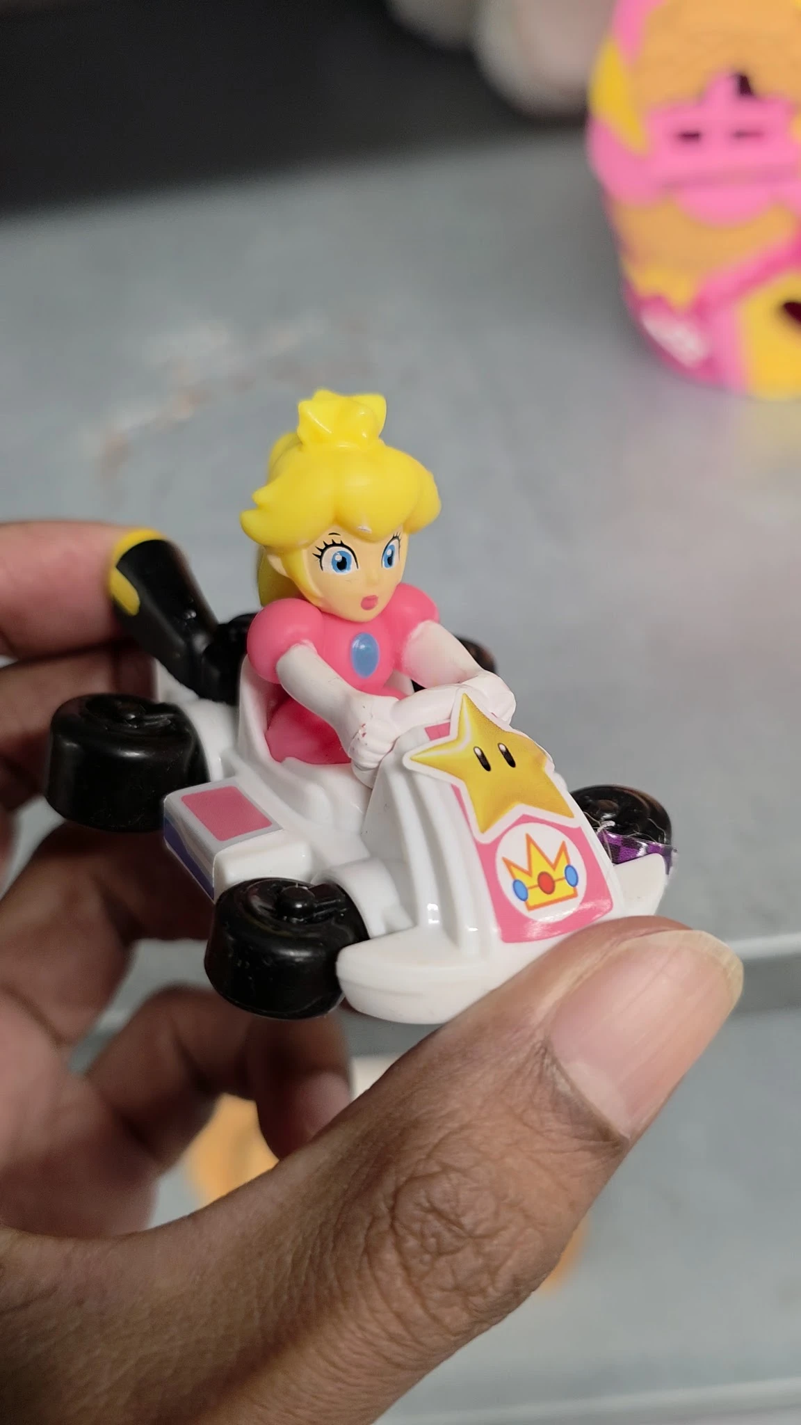 Close-up van een speelgoedfiguur: Prinses Peach uit Mario Kart in een roze racewagen