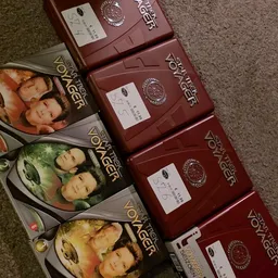 Stapel dvd-boxen van de serie Dawson's Creek in rood, links enkele dvd-hoezen op de grond