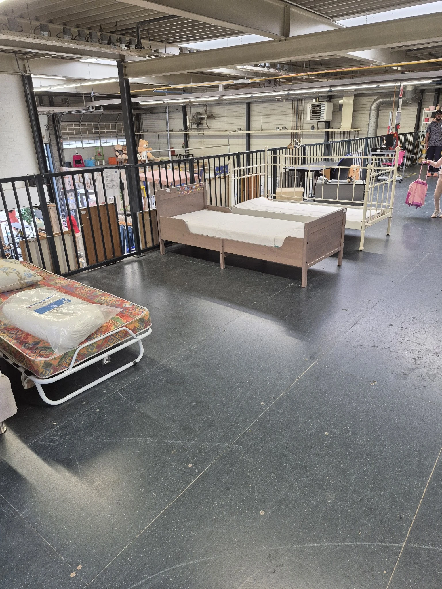 Uitgestalde bedden en matrassen in de kringloopwinkel, waaronder een opvouwbaar bed op de voorgrond
