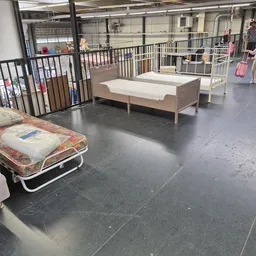 Uitgestalde bedden en matrassen in de kringloopwinkel, waaronder een opvouwbaar bed op de voorgrond