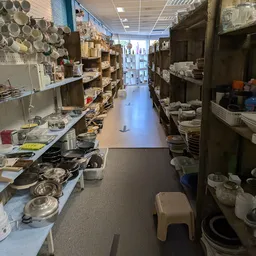 Lange gang in kringloopwinkel met stellingen vol servies, pannen en huishoudartikelen aan beide zijden