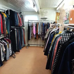 Winkelvloer met kledingrekken vol tweedehands kleding, rode zijkant links, lampen aan plafond