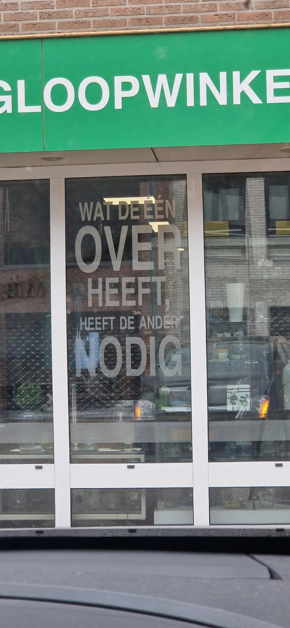 Winkelruit met wit raamlettering 'WAI DE EEN OVER HEEFT, HEEFT DE ANDER NODIG'