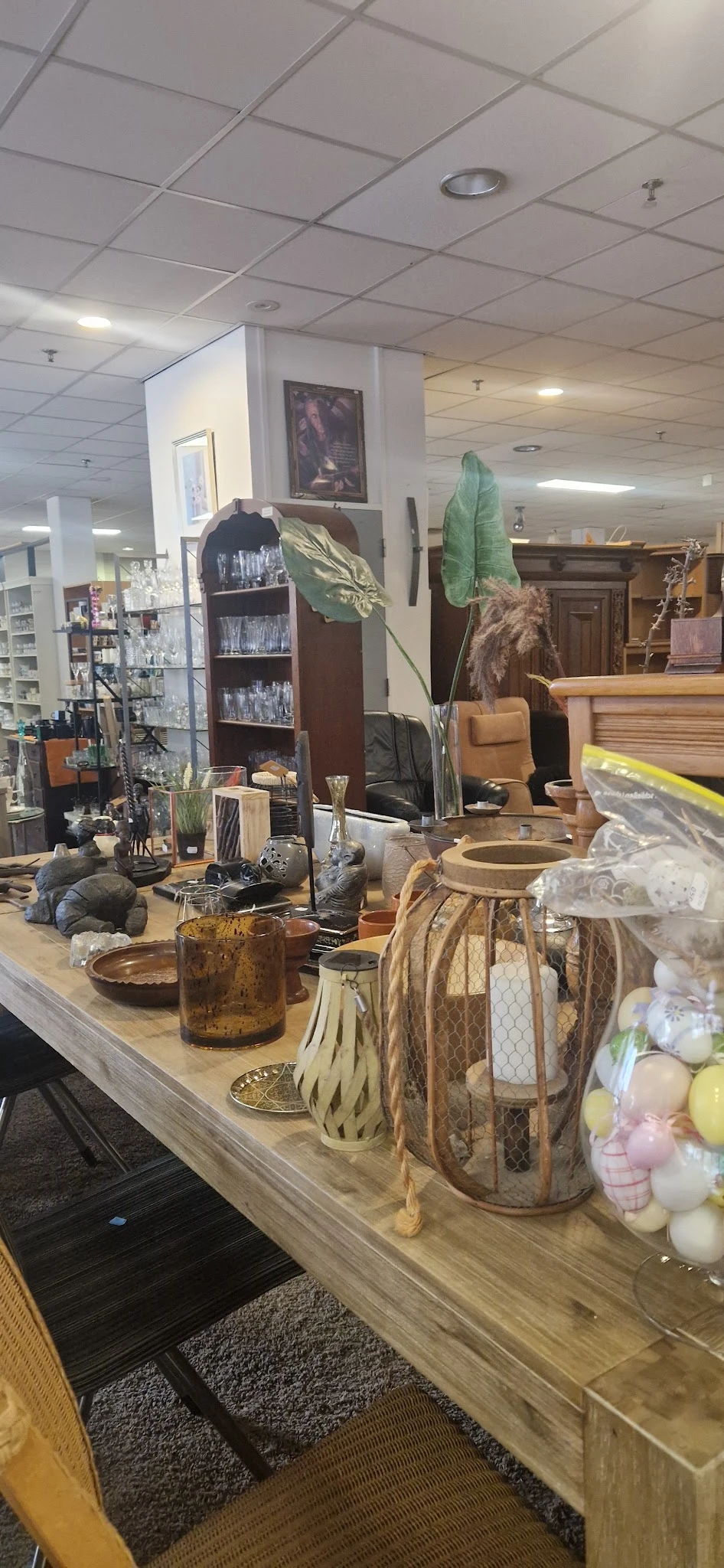 Uitgestalde decoratieve items en huishoudspullen op toonbank: glazen, vazen, plantenpotten, kussentjes en diverse woonaccesso