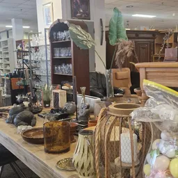 Uitgestalde decoratieve items en huishoudspullen op toonbank: glazen, vazen, plantenpotten, kussentjes en diverse woonaccesso