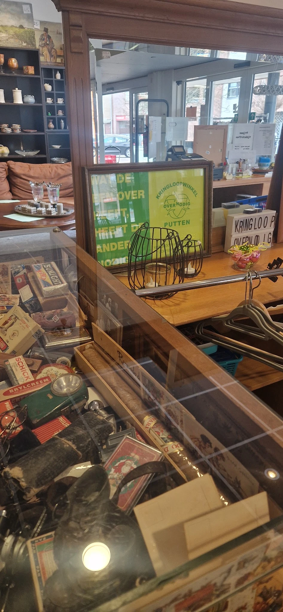 Houten kastplank met verschillende huishoudartikelen: groen draadmand, metalen hangers, bloempot en dozen.