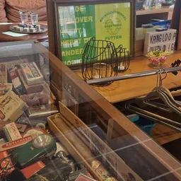 Houten kastplank met verschillende huishoudartikelen: groen draadmand, metalen hangers, bloempot en dozen.