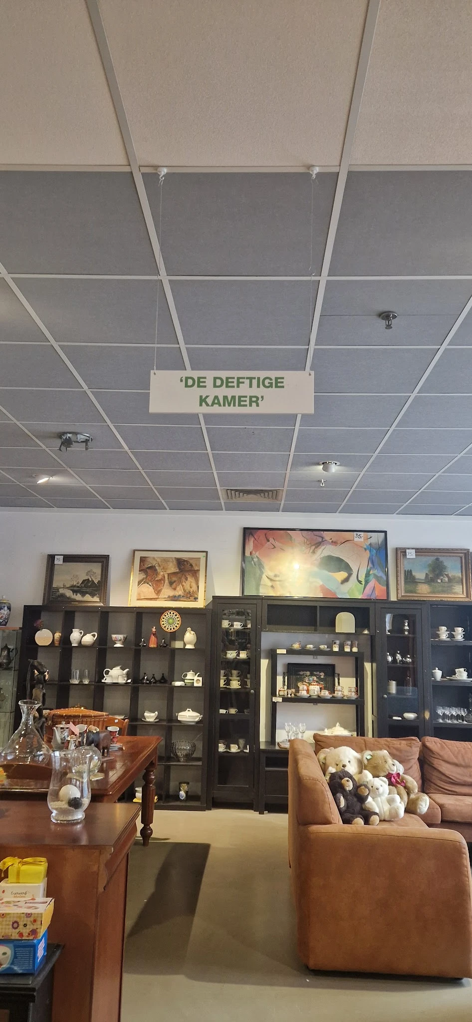 Winkelinterieur met plafond, zwarte vitrinekast met porselein en decoratie, schilderijen aan de muur.