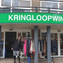 Groene gevel van kringloopwinkel met uitstalraam met kleding, persoon in zwarte jas voor de ingang